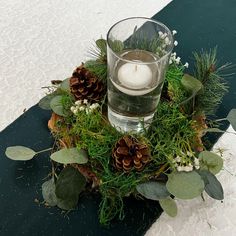 a candle is sitting on top of a table with greenery and pineconis