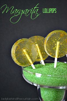 three lollipops sitting in a glass bowl with green and yellow toppings