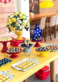 a yellow table topped with lots of desserts and flowers next to a vase filled with flowers