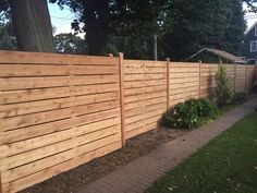 a wooden fence next to a brick walkway in front of a tree and grass area