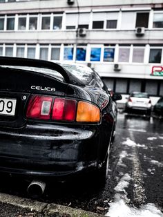 the back end of a black car parked in front of a building on a snowy day