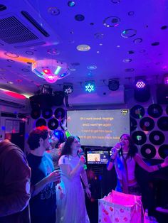 a group of people standing in front of a projector screen at a party with lights on