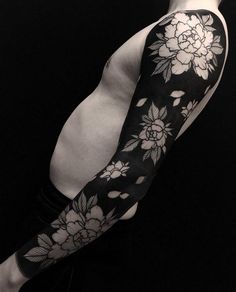 a man's arm covered in black and white tattoos with flowers on the sleeve