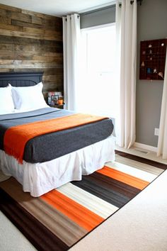 the bed is made and has an orange, black, gray and white blanket on it