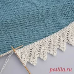 a blue and white knitted blanket next to a pair of knitting needles