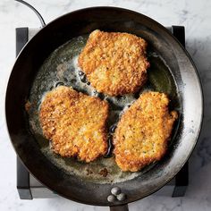 three fried meat patties cooking in a frying pan on a stove burner