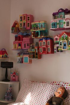 there is a doll sitting on the bed in front of many toy houses hanging from the wall