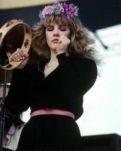 a woman standing in front of a microphone with her hand on her face and wearing a flower crown