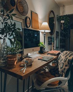 a desk with a computer on top of it next to a lamp and potted plants