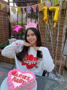 a woman sitting at a table with a heart shaped cake and balloons in the background