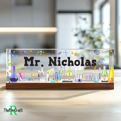 a glass sign that says mr nicholas in front of some flasks and beakets