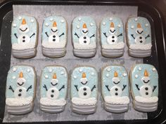 decorated cookies in the shape of snowmen with frosting on them, are sitting in a baking pan