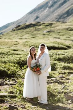 two brides standing in the mountains posing for a photo