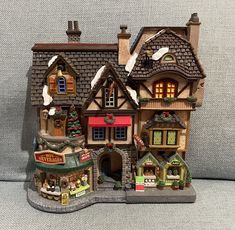 a toy house with christmas decorations on the roof and windows, in front of a gray background