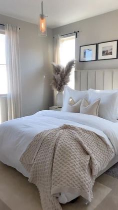 a bed with white linens and pillows in a bedroom next to two framed pictures on the wall