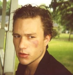 a close up of a person wearing a black shirt and looking at the camera with trees in the background