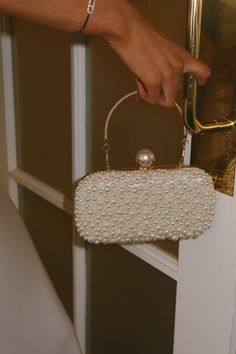 DETAILS: Our Pearl Bead Chic Clutch/Crossbody Bag In White is a outstanding detailed bag with a gold metal strap handle and a alternative metal link crossbody strap. The bag has a big pearl detail closure on the center top and pearl embellishments on the front and a silver shimmer fabric on the backside. DIMENSIONS: 7.5 X 2 X 3.75 Crossbody Evening Bag With Pearl Handle, Formal Crossbody Bag With Pearl Handle, White Party Bags With Gold-tone Hardware, Gold Crossbody Shoulder Bag With Pearl Handle, Elegant Pearl Handle Crossbody Evening Bag, Elegant Crossbody Evening Bag With Pearl Handle, Formal Crossbody Evening Bag With Pearl Handle, Handheld Clutch With Pearl Handle, Formal Bags With Pearl Chain