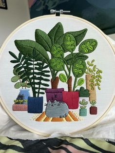 a cat sitting in front of a potted plant on top of a table next to a wall hanging