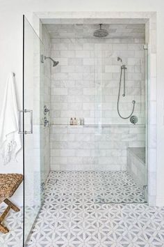 a walk in shower sitting next to a white tiled wall and floor with a bench