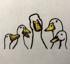 three ducks with yellow beaks on a white cloth textured background that is embroidered onto the fabric