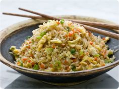 a bowl filled with rice and vegetables next to chopsticks on a marble table