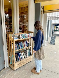 a woman standing in front of a book store looking at books on a wooden shelf