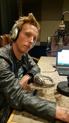 a man wearing headphones sitting at a table with a laptop computer and microphone in front of him