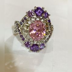 What A Pretty Ring!! Surrounding A Large Clear ‘Pink’ Stone Is Pretty Flower Like Metal Work. 3 Purple Gemstones Complete The Top And Bottom Of The Ring. Tiny Purple Gemstones Flank Each Side. There Is A Marking On The Inside Of The Ring, However I Can’t Decipher It, So I’m Selling It As Costume Jewelry. Very Good Condition. Never Worn. Pink Crystal Ring With Accent Stones In Cubic Zirconia, Pink Crystal Ring With Sparkling Stones For Gift, Pink Oval Crystal Ring With Cubic Zirconia, Pink Oval Cubic Zirconia Crystal Ring, Pink Ring With Sparkling Stones, Pink Oval Feminine Jewelry, Feminine Oval Pink Jewelry, Feminine Pink Oval Jewelry, Pink Stone Ring Jewelry