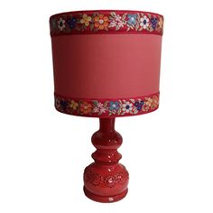 a red table lamp with a pink shade on it's base and flowered trim around the top