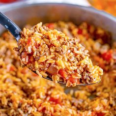 a spoon full of mexican rice with tomatoes and meat on it, being lifted from a skillet