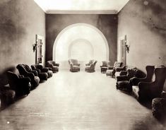 an old black and white photo of chairs in a large room with arched doorways