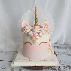 a pink and white birthday cake with a unicorn horn on it's top, sitting on a wooden stand