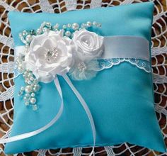 a blue ring pillow with white flowers and pearls on the sash is sitting on a lace doily