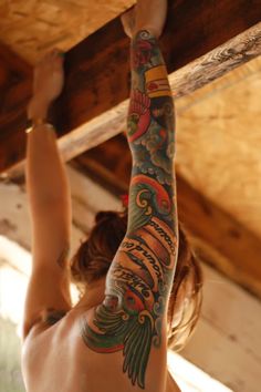 a woman with tattoos on her arm and arms reaching up to the ceiling above her head