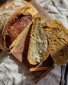 a sliced loaf of bread sitting on top of a cutting board next to cinnamon sticks