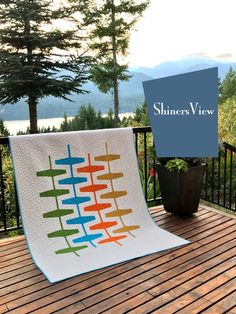 a colorful quilt sitting on top of a wooden deck next to a potted plant