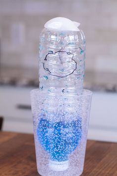 a plastic water bottle sitting on top of a wooden table next to a blue and white cup