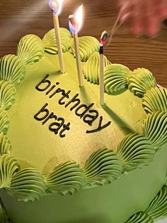 a birthday cake with green frosting and lit candles on it that reads, birthday brat