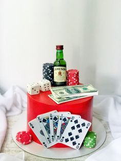 a red cake with playing cards, dices and a bottle on the table next to it