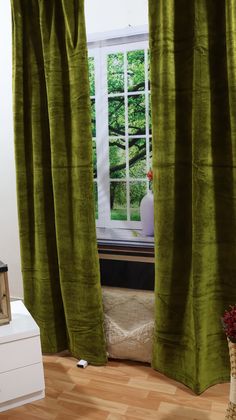 a green curtain hanging in front of a window next to a white chest of drawers