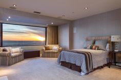 a bedroom with a large bed and two chairs in front of a window overlooking the ocean