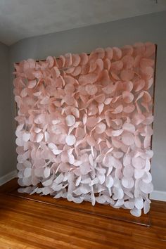 a large piece of art made out of paper flowers on a wooden floor in front of a gray wall