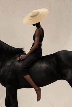 a woman sitting on the back of a black horse wearing a straw hat and dress