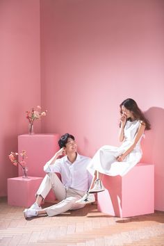 a man and woman sitting on pink cubes talking on their cell phones in front of a pink wall