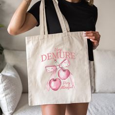 Carry the viral TikTok trend with our Very Demure Tote Bag! This cotton canvas bag features adorable coquette cherries with a pink bow paired with the "Very Demure, Very Mindful" phrase that's taken over TikTok. Perfect for coquette lovers and anyone who's all about that girly vibe, this tote is a must-have for your daily essentials. Whether you're treating yourself or gifting it to a friend, this bag is the perfect way to carry your essentials in style. Snag yours now and stay on trend! Key Fea Trendy Cotton Shoulder Bag Gift, Trendy Cotton Bags For Gifts, Trendy Beige Canvas Bag For Gift, Cute Pink Tote Bag, Trendy Pink Canvas Bag As Gift, Pink Girly Stuff, Trendy Pink Canvas Bag For Gift, Trendy Pink Tote Bag, Croquette Tote Bag