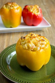 two stuffed peppers sitting on top of a green plate next to a white plate filled with food