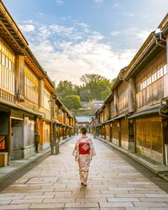 a woman in kimono walking down an alley way with shops on both sides and buildings to the side