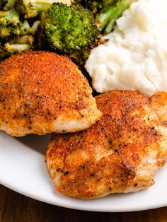 two pieces of chicken, mashed potatoes and broccoli on a white plate