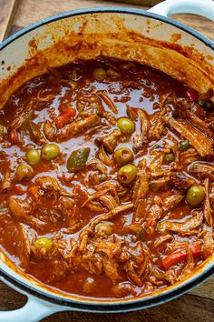 a pot filled with meat and olives on top of a wooden table