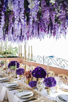 the table is set with purple and white flowers hanging from it's rafters